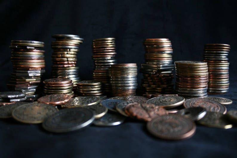 Peut inclure: Une collection de pi&egrave;ces de monnaie empil&eacute;es de diff&eacute;rentes tailles et couleurs, notamment or, argent et cuivre. Les pi&egrave;ces sont dispos&eacute;es en rang&eacute;e sur une surface sombre.