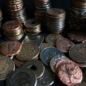 Peut inclure: Une collection de pi&egrave;ces de monnaie en m&eacute;tal de diff&eacute;rentes tailles et formes avec des motifs complexes. Les pi&egrave;ces sont dispos&eacute;es en pile sur une surface noire.