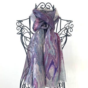 May include: A purple and grey silk scarf with a marbled pattern. The scarf is tied around a black metal mannequin.