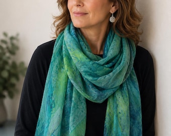 May include: A lightweight rectangular scarf featuring a marbled pattern in shades of teal, emerald green, and lime green. The scarf has a soft, semi-sheer texture with delicate frayed edges along the bottom hem, worn over a solid black long-sleeve top.