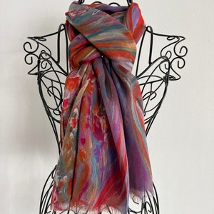 A colorful silk modal scarf with a fringed edge by KayJayStudio. The scarf has a pattern of orange, purple, blue, and brown stripes and swirls.