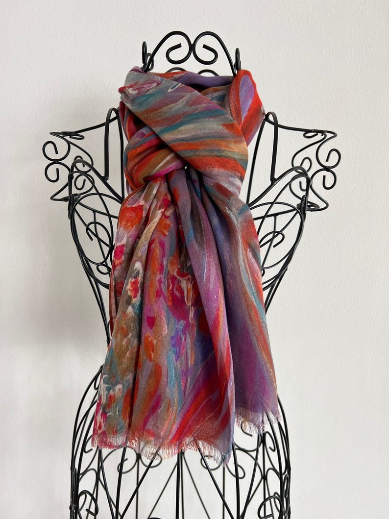 A colorful silk modal scarf with a fringed edge by KayJayStudio. The scarf has a pattern of orange, purple, blue, and brown stripes and swirls.