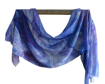May include: A lightweight scarf featuring a swirling abstract pattern in shades of deep indigo, royal blue, violet, and white. The fabric displays a fluid, marbled design with soft gradients and light-colored speckles throughout the material.