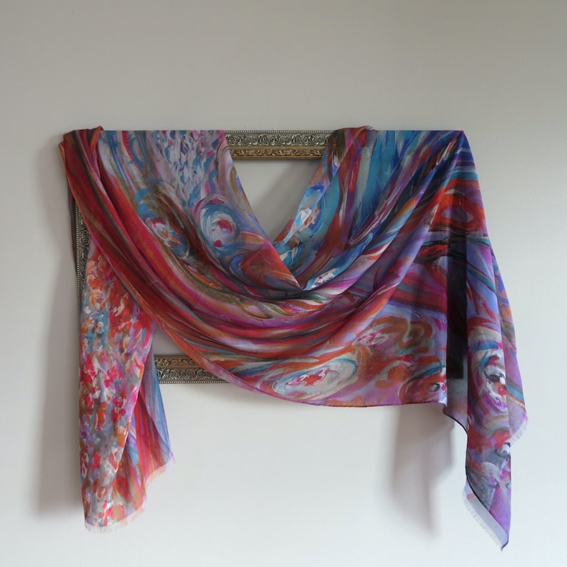 A colorful silk modal scarf by KayJayStudio with a swirling abstract pattern in shades of red, orange, blue, purple, and white. The scarf is draped over a gold picture frame displaying artful elegance.