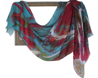 Puede incluir: Un pañuelo rectangular ligero con un patrón abstracto en tonos vibrantes de turquesa, rojo intenso y blanco. La tela está drapeada sobre un marco rectangular ornamentado de tono metálico, mostrando la textura fluida del material.