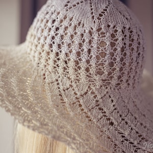 May include: A white crocheted sun hat with a delicate lace pattern. The hat is made of fine yarn and has a wide brim.
