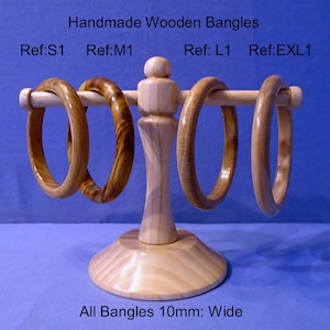 Puede incluir: Exhibición de cuatro brazaletes de madera hechos a mano, cada uno con patrones de vetas y tonos únicos, presentados en un soporte de madera clara. El texto "Handmade Wooden Bangles" y los números de referencia son visibles. Todos los brazaletes tienen 10 mm de ancho.