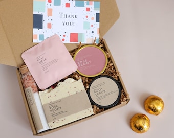 May include: A gift box filled with bath and body products, including a clay mask, bath salts, soap, body scrub, and bath bombs. The box is open and the products are visible. The box is decorated with a thank you card.
