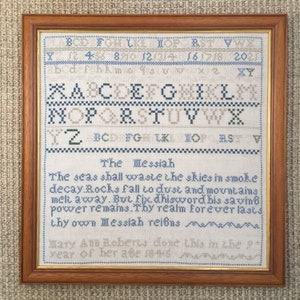 Op de afbeelding: Een ingelijst borduurwerk met een blauw en wit alfabet, een vers over de Messias en de tekst "Mary Am Roberts done this in the 9 year of her age 1845".
