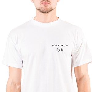 Peut inclure: T-shirt blanc avec un imprimé noir qui dit "Papa d'Amour" et "A&M" dans un style manuscrit.