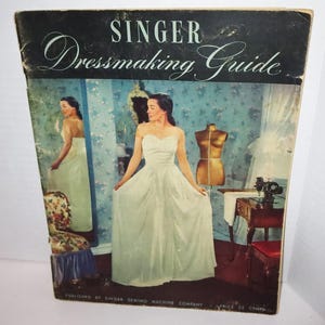 May include: Vintage Singer Dressmaking Guide book cover. The cover features a woman in a white strapless gown, a dress form, and a sewing machine. The title is in elegant script. The background has a floral wallpaper design.