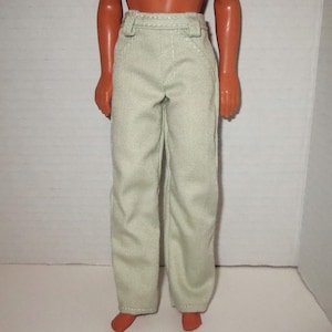 May include: A pair of light beige, straight-leg trousers with a visible diagonal twill weave pattern. The pants feature a structured waistband with belt loops and a clean, minimalist design, worn on a doll figure with orange-toned skin.