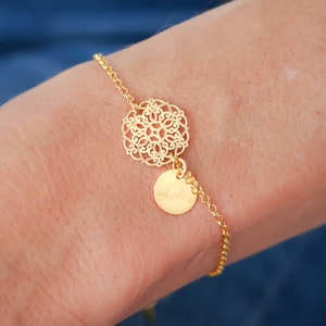 Könnte beinhalten: Ein goldenes Kettenarmband mit einem filigranen Anhänger und einem runden Anhänger mit einer Inschrift.