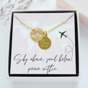 Könnte beinhalten: Goldkette mit einem Weltkarten-Anhänger und einem runden Anhänger mit der Aufschrift "Mexiko Juni 2022". Die Kette befindet sich in einer weißen Schachtel mit rosa Innenausstattung und dem Text "Sky above, sand below, peace within".