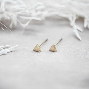 Könnte beinhalten: Ein Paar goldene Dreiecks-Ohrstecker auf weißem Hintergrund.