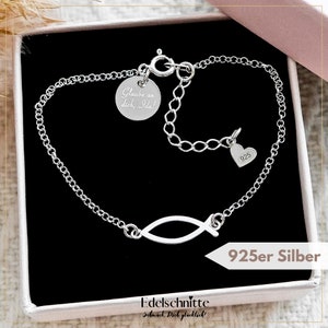 Op de afbeelding: Een zilveren kettingarmband met een klein visje bedel en een hartbedel met de inscriptie "925". De armband zit in een klein doosje met de tekst "Edelschnitte" en "Schmuck Dich glücklich!" erop.