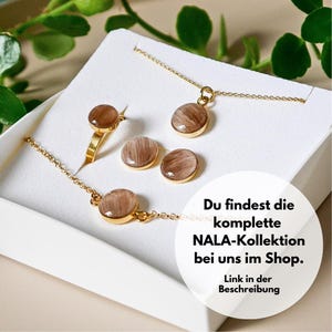 Op de afbeelding: Een set gouden sieraden met een ketting, armband, ring en oorbellen. Elk stuk heeft een ronde hanger met een bruin en wit swirl-patroon. De tekst "Du findest die komplette NALA-Kollektion bei uns im Shop. Link in der Beschreibung" is zichtbaar in de afbeelding.