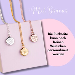 Op de afbeelding: Drie gouden kettingen met ronde hangers. De hangers zijn gegraveerd met de namen "Fanny", "Momo & Baghira" en een hart met een pootprint. De tekst "Mit Gravur" is in cursief boven de kettingen geschreven. De tekst "Die R&uuml;ckseite kann nach Deinen W&uuml;nschen personalisiert werden" is onder de kettingen geschreven.