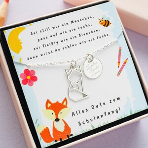K&ouml;nnte beinhalten: Eine silberne Halskette mit einem Fuchs-Anh&auml;nger und einem runden Anh&auml;nger mit der Aufschrift "Schlau Fuchs Lena". Die Halskette befindet sich in einer wei&szlig;en Schachtel mit einer bunten Illustration eines Fuchses und dem Text "Sei still wie ein M&auml;uschen, pass auf wie ein Luchs. Sei flei&szlig;ig wie ein Bienchen. Dann wirst Du schlau wie ein Fuchs. Alles Gute zum Schulanfang!"