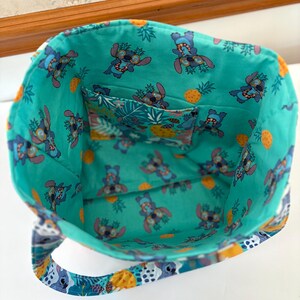 May include: A turquoise tote bag with a colorful interior featuring a cartoon character wearing sunglasses and pineapples. The bag has a matching interior pocket and handles with a patterned design. The bag is open, showing the inside.