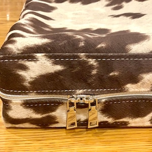 May include: A brown and white cowhide dog bed with a zipper closure.