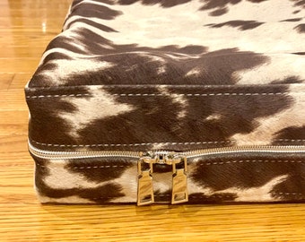 May include: A brown and white cowhide dog bed with a zipper closure.