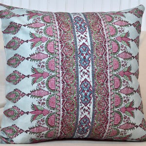 May include: Square decorative pillow with a light blue background and a central vertical stripe design. The design features pink, green, and blue floral and geometric patterns. The pillow is a square shape.