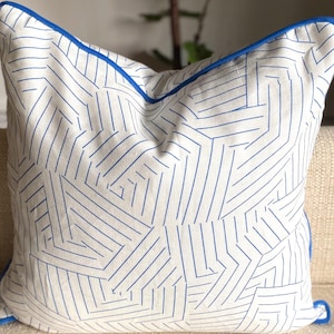 May include: A white throw pillow with a geometric pattern of blue lines. The pillow has a blue trim around the edges.