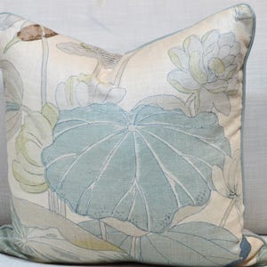 Puede incluir: Una almohada decorativa con un patrón floral de color azul claro y blanco con flores y hojas de loto. La almohada está hecha de una tela suave y texturizada.
