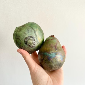 Puede incluir: Dos peras de cerámica, una verde con detalles dorados y la otra verde con detalles iridiscentes.