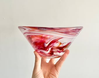 May include: A clear glass bowl with a swirl pattern in shades of pink, white, and orange. The bowl is slightly tilted and has a small sticker on the bottom.