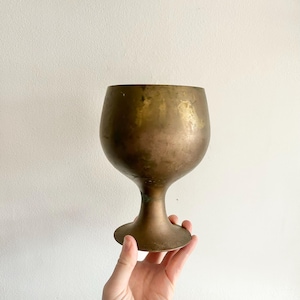May include: A vintage brass goblet with a wide, round bowl and a short, flared stem. The goblet has a worn, aged finish.