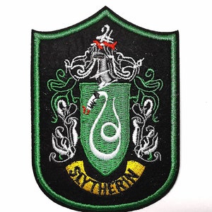 Op de afbeelding: Geborduurde patch met het Slytherin-embleem uit de Harry Potter-serie. De patch heeft een zwarte achtergrond met een groene rand. Het embleem bevat een groen schild met een witte slang en het woord "Slytherin" in geel.