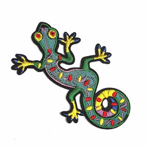 May include: Embroidered patch depicting a green lizard with a curled tail. The lizard has yellow, red, and blue detailing, with a black border. The design is set against a white backdrop. Suitable for application on clothing or accessories.