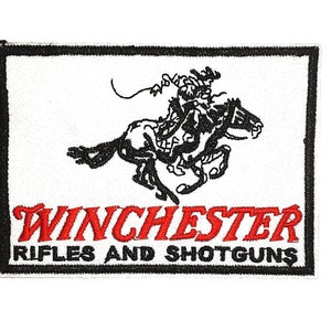 Puede incluir: Parche bordado con la silueta negra de un vaquero a caballo, con un lazo. La palabra "WINCHESTER" es roja, con "RIFLES AND SHOTGUNS" debajo, todo sobre un fondo blanco con un borde negro.