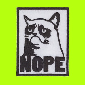Puede incluir: Parche rectangular con una ilustración en blanco y negro de un gato gruñón. La palabra "NOPE" está impresa en letras mayúsculas negras debajo de la cara del gato. El parche tiene un borde negro y está sobre un fondo verde brillante.