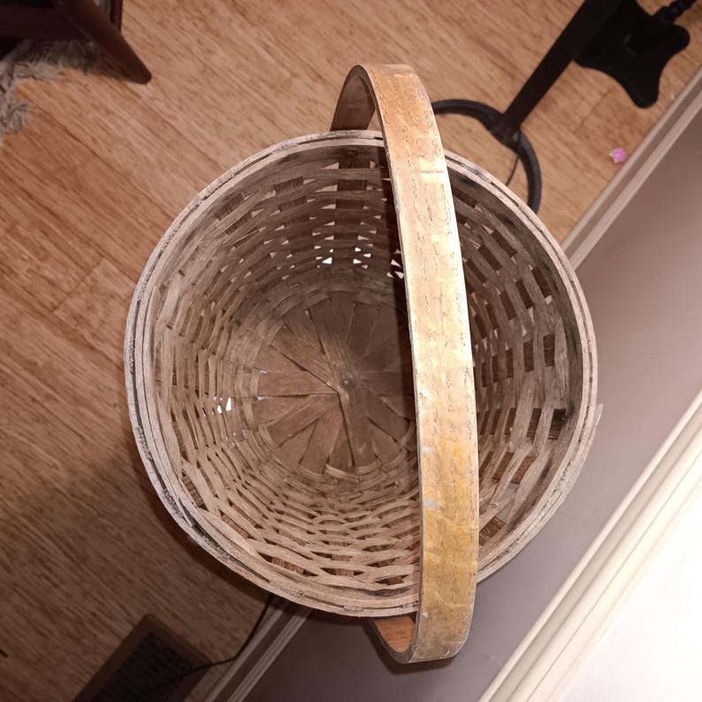 May include: A round, woven basket with a sturdy handle. The basket is made of light-colored wood and has a circular shape. The handle is made of the same material and is attached to the top of the basket. The basket is empty.