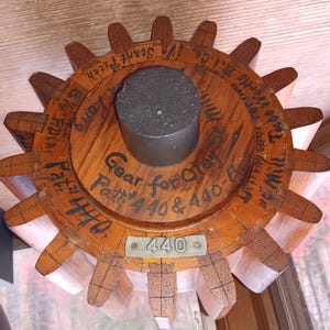 May include: A wooden gear with a central metal cylinder. The gear has multiple teeth and is inscribed with text, including "Gear for Oley" and "Patt. #440 & 440-F." A small metal plate reads "440."