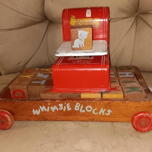 May include: Vintage wooden toy with red wheels and a red metal scale. The toy has a wooden base with alphabet blocks and the words "WHIMSIE BLOCKS" painted on the side. A wooden block with a cat image sits on the scale.