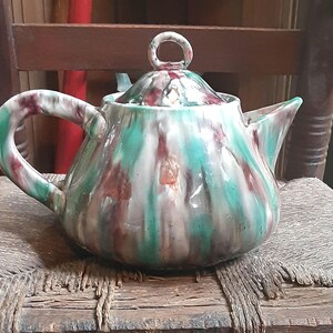 以下が含まれることがあります： 緑、白、茶色の釉薬をかけたセラミック製のティーポット。ティーポットは丸いボディとリングハンドルが付いた蓋をしています。