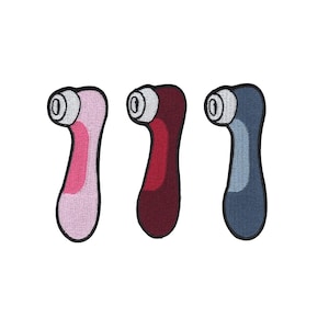 Può includere: Tre toppe ricamate a forma di un dispositivo stilizzato. Le toppe sono rosa, bordeaux e blu, ciascuna con un dettaglio circolare bianco e nero. Le toppe hanno un bordo nero.