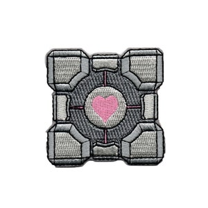 Peut inclure: Un patch brodé gris et blanc représentant un cube stylisé avec un cœur rose au centre. Le cube a un motif en grille et une ouverture circulaire avec un cœur rose au centre.
