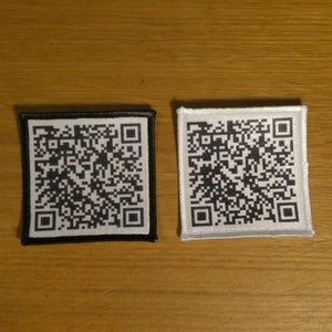 May include: Two square fabric patches with black and white QR codes. The patch on the left has a black border and a white QR code. The patch on the right has a white border and a black QR code.