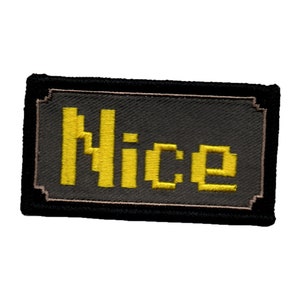 May include: A black embroidered patch with a yellow pixelated word "Nice" on a grey background.