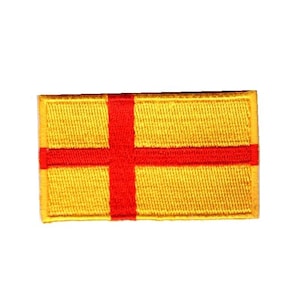 以下が含まれることがあります： 金色の背景に赤い十字が描かれた長方形のパッチ。パッチにはステッチされた縁があり、質感があります。十字は中央に配置され、パッチの幅と高さ全体に広がっています。