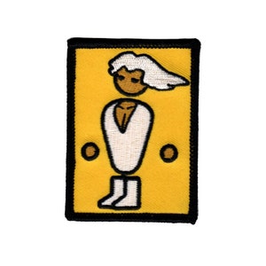 Può includere: Una toppa ricamata gialla con bordo nero che presenta una figura stilizzata bianca con capelli bianchi, che indossa una camicia bianca e stivali bianchi. La figura stilizzata ha la pelle marrone e sta in piedi con le braccia lungo i fianchi.