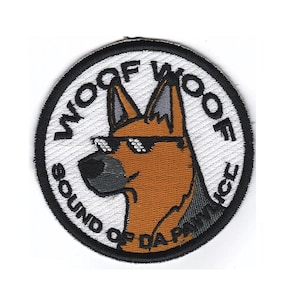Puede incluir: Un parche redondo bordado en blanco y negro con un pastor alemán de dibujos animados que lleva gafas de sol. El texto "Woof of Woof" está escrito alrededor de la cabeza del perro, y el texto "Sound of Da Pack" está escrito debajo de la cabeza del perro.