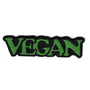以下が含まれることがあります： 「VEGAN」という単語が太字でスタイリッシュなフォントで書かれた緑色の刺繍パッチ