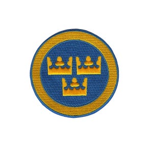 Pode incluir: Um remendo bordado azul e dourado com três coroas douradas dentro de um círculo.