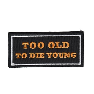 May include: Black embroidered patch with white border and orange text that reads "Too Old To Die Young".